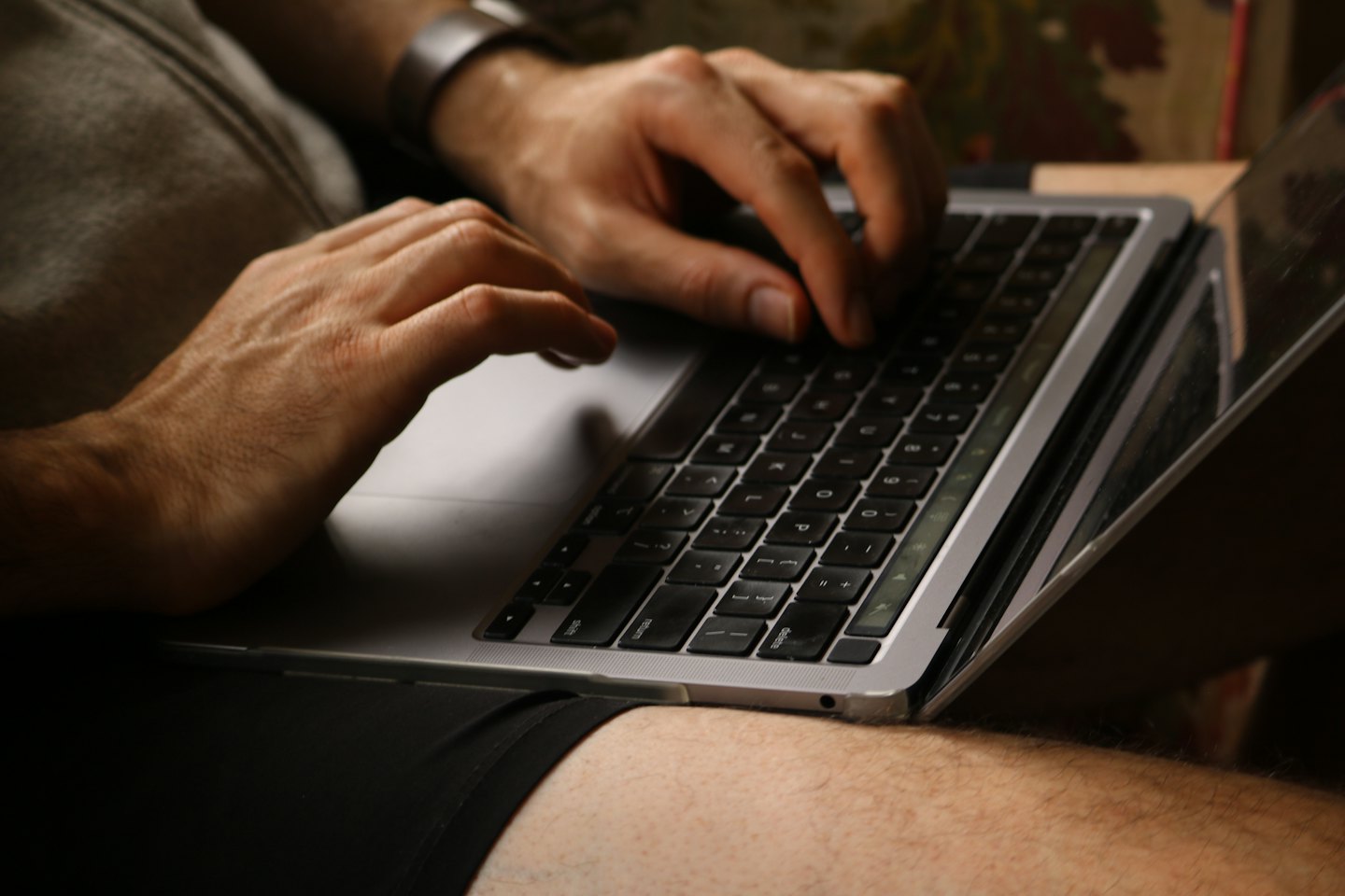 Mani che digitano su un laptop argentato appoggiato sulle ginocchia.